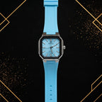 Elegance luxury men's quartz watch featuring a sky blue textured horizontal dial, polished silver stainless steel octagonal case with a black bezel, and a matching sky-blue silicone strap, shown in a straight front view against a black and gold luxury background.