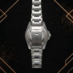 Back view of a stainless steel sports watch showing the brushed solid caseback, crown logo engraved folding clasp, and link structure.