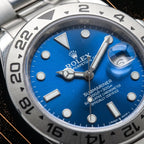 Extreme close-up of a vibrant blue watch dial displaying luminescent hour markers, Mercedes hands, date magnification window, and engraved bezel numbers.