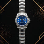 Front centered view of a Rolex Submariner watch with a vibrant blue sunburst dial, engraved stainless steel bezel, date cyclops window, and steel oyster bracelet on a dark patterned background.