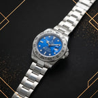 45-degree angled view of a luxury stainless steel sports watch featuring a sunburst blue dial, engraved steel bezel, and oyster bracelet on a dark luxury background.