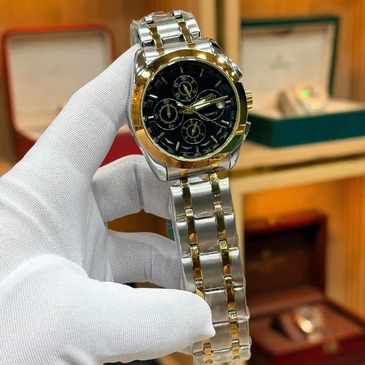 Tissot Chronograph Two-Tone Gold and Silver Men's Watch with Black Dial, Date Display, and Tachymeter Bezel, held by a gloved hand