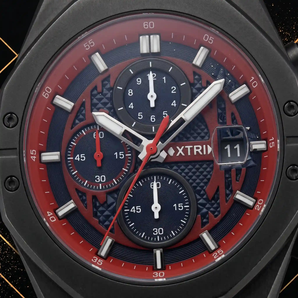 Macro close-up shot of XTRI watch dial showing chronograph subdials, red chapter ring, hour markers, and date aperture framed by luxury black and gold elements.