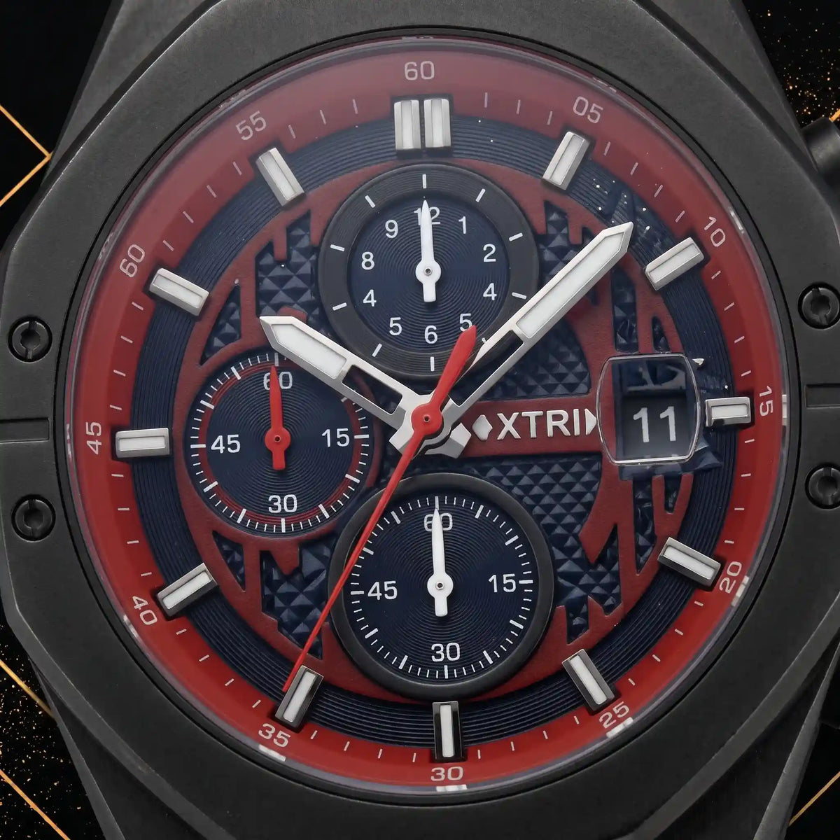 Macro close-up shot of XTRI watch dial showing chronograph subdials, red chapter ring, hour markers, and date aperture framed by luxury black and gold elements.